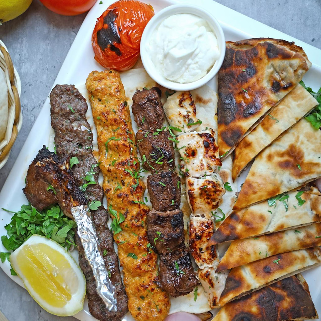 A generous spread of grilled lamb, chicken, and kofta skewers, served with warm flatbread, roasted tomato, and garlic yogurt.