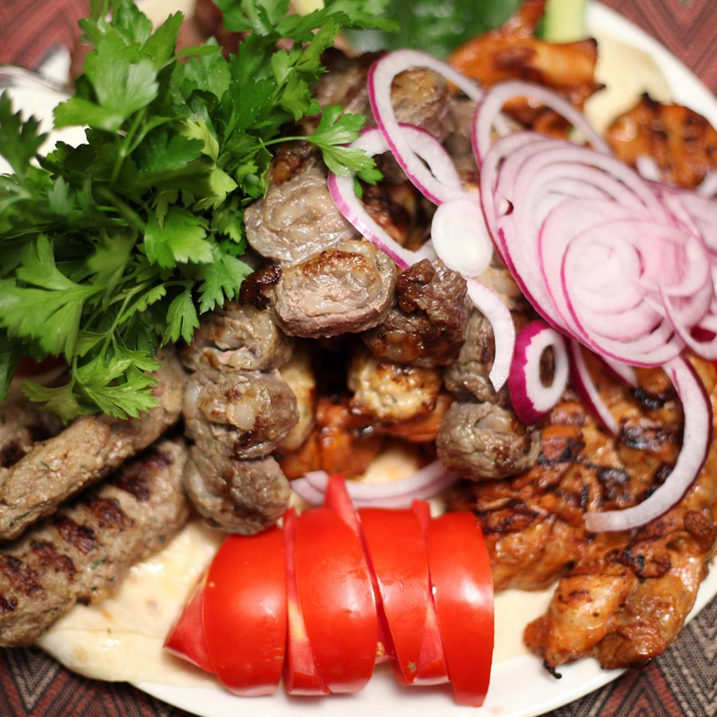 A feast of grilled lamb cubes, spiced kofta, and marinated chicken, topped with fresh herbs, red onion, and sliced tomato.
