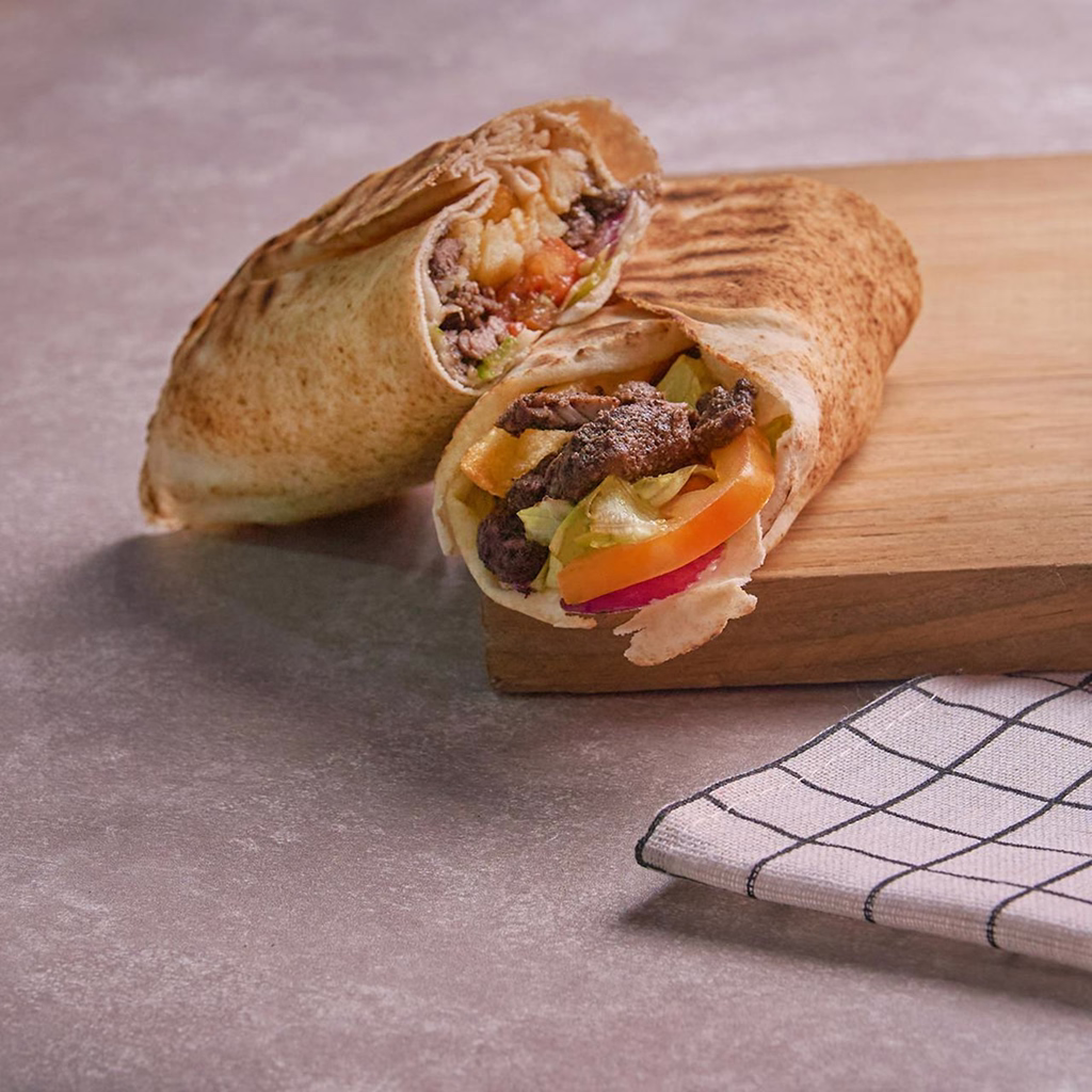 Toasted flatbread filled with seasoned grilled beef strips, crisp lettuce, fresh tomato, and tangy pickled vegetables.