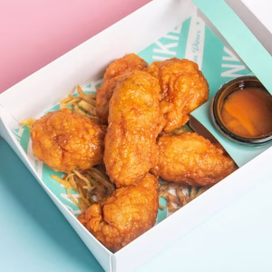 Five spicy fried chicken wings served in a box with hot sauce and potato straws.
